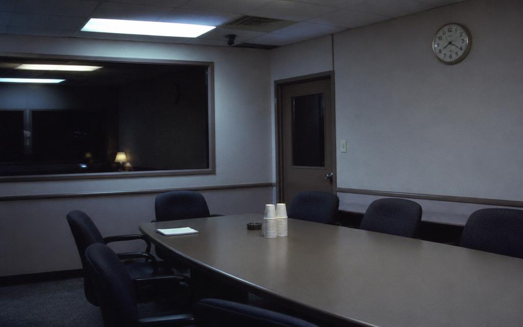 Empty focus group facility room at night with a one-way mirror and wall clock