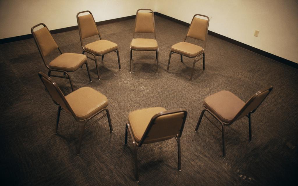 A small circle of eight empty chairs in a plain meeting room